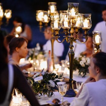 Decorated tables with floral composition and old fashioned candlesticks and guests in the celebration evening